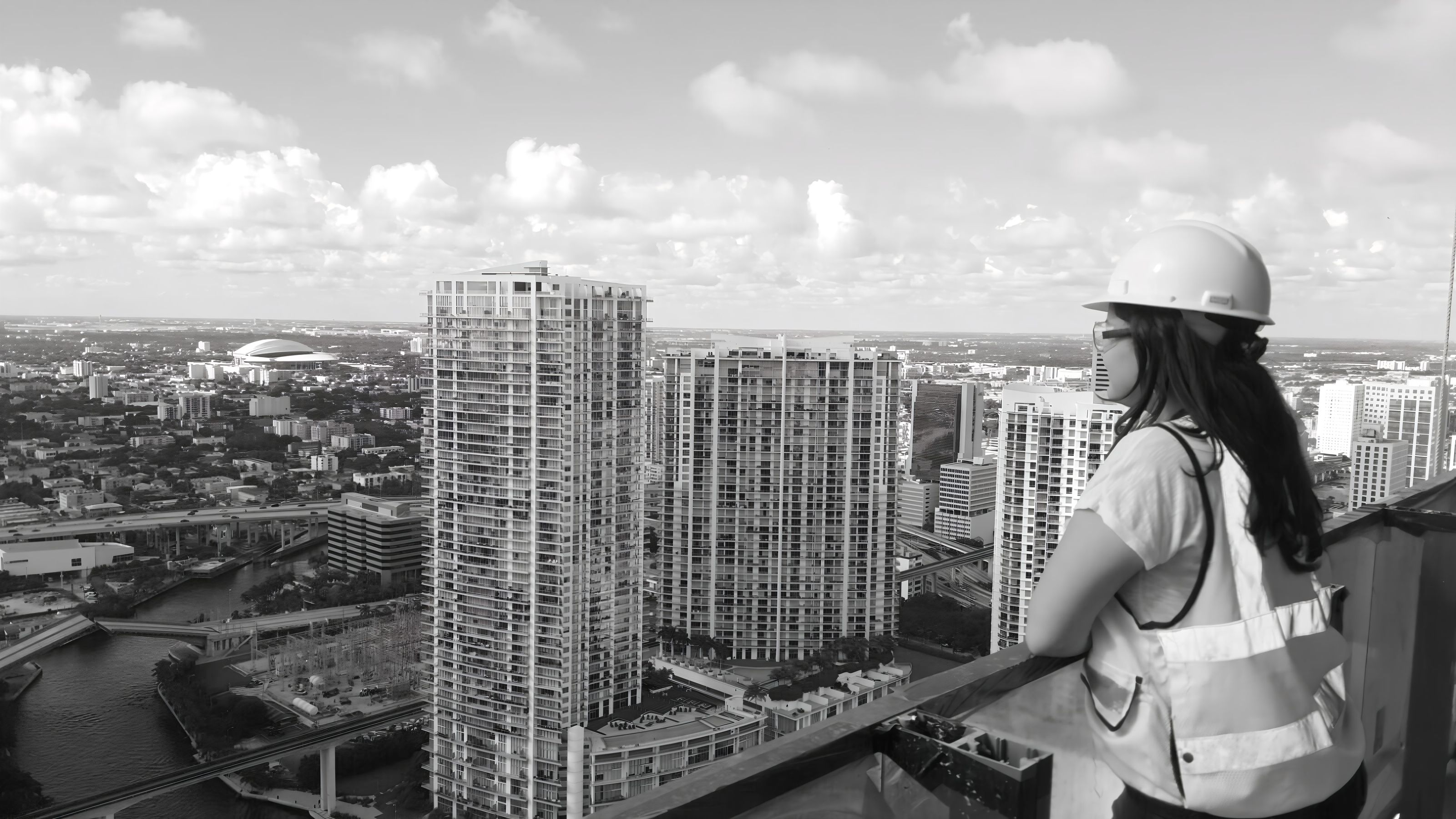 Ruth Narváez con casco y chaleco sobre una azotea, frente a un horizonte de torres, en blanco y negro