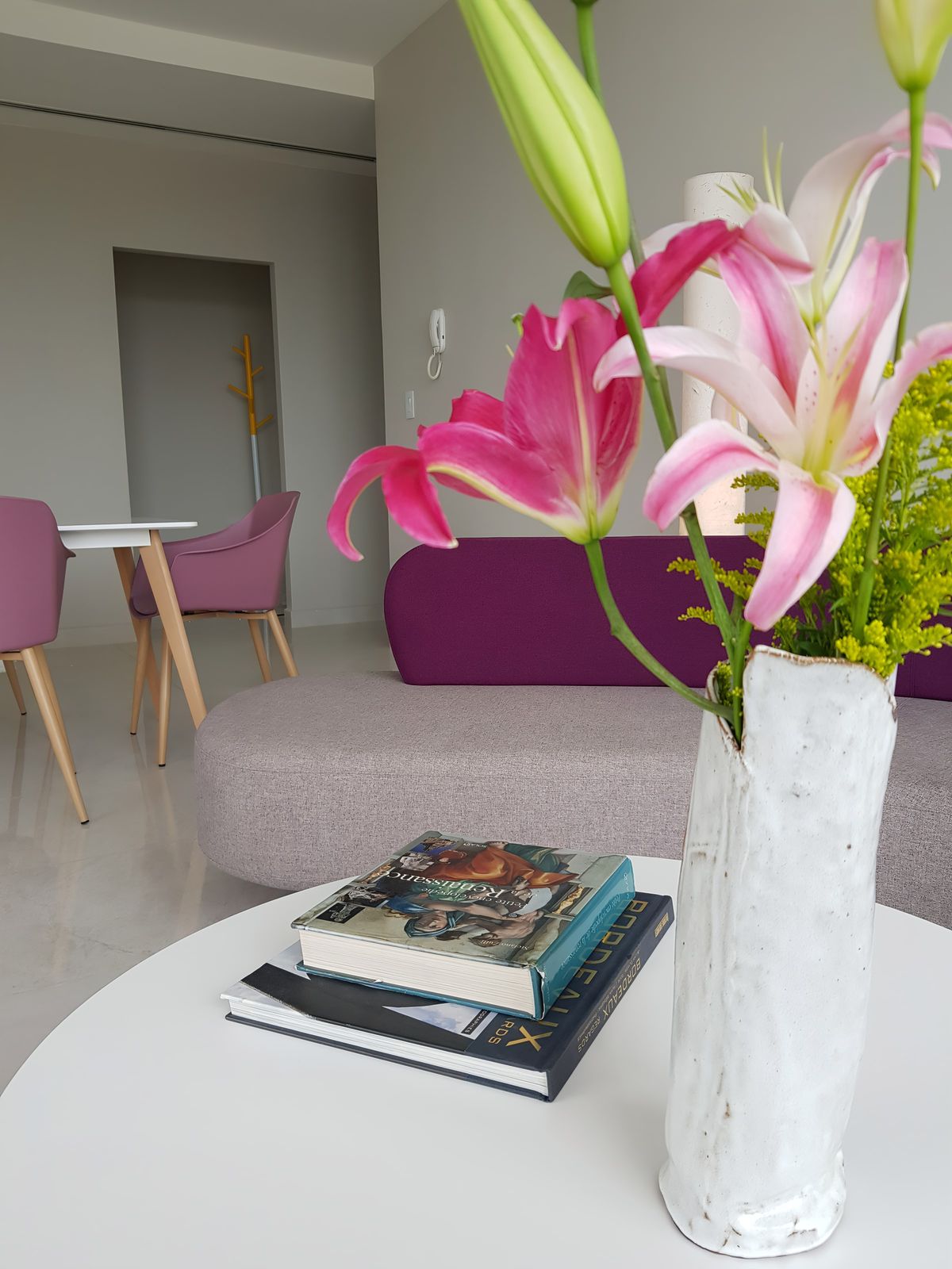 Mesa blanca con flores rosadas y libros, sillas malva al fondo