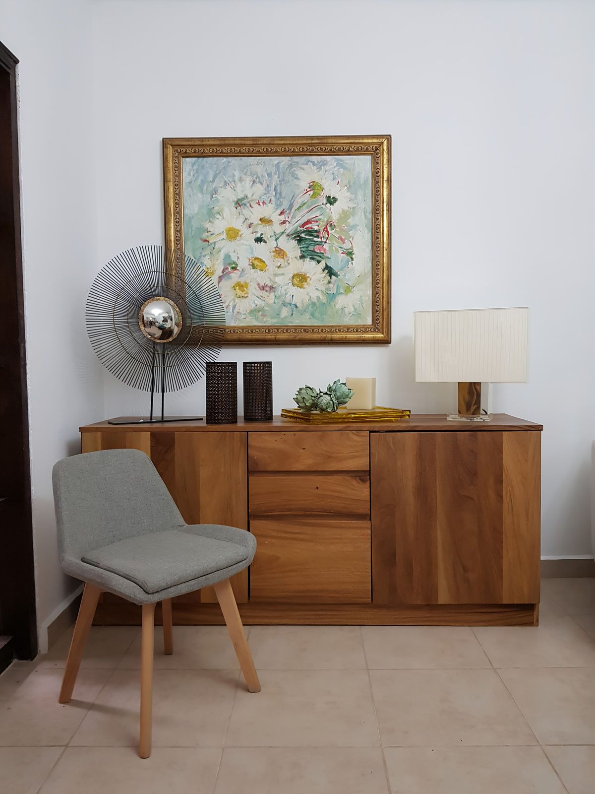 Aparador de madera con cuadro floral, lámpara y silla gris