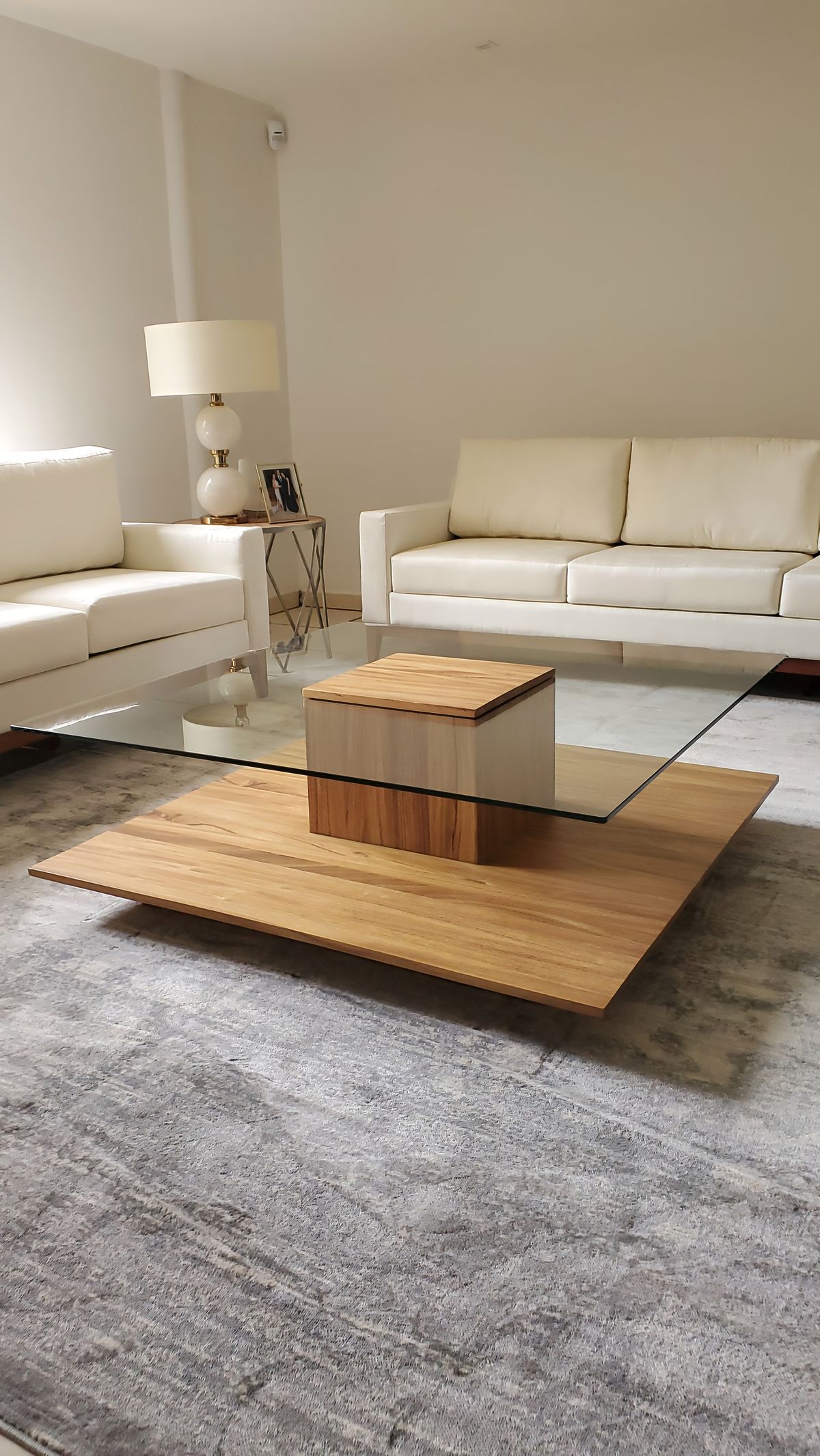 Sala en crema con mesa de centro de madera y vidrio sobre alfombra gris