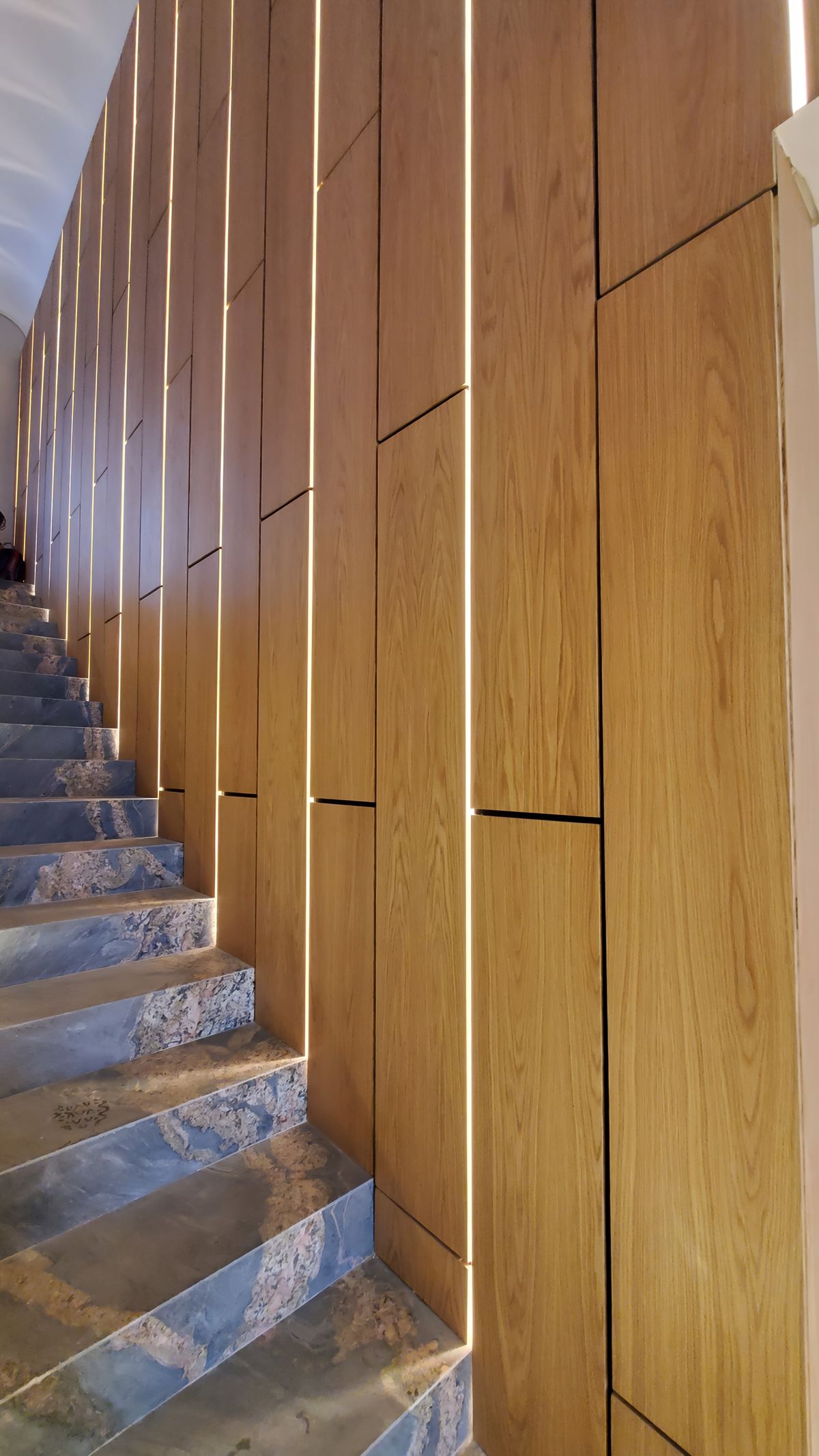 Escalera con revestimiento de madera vertical y peldaños de piedra veteada